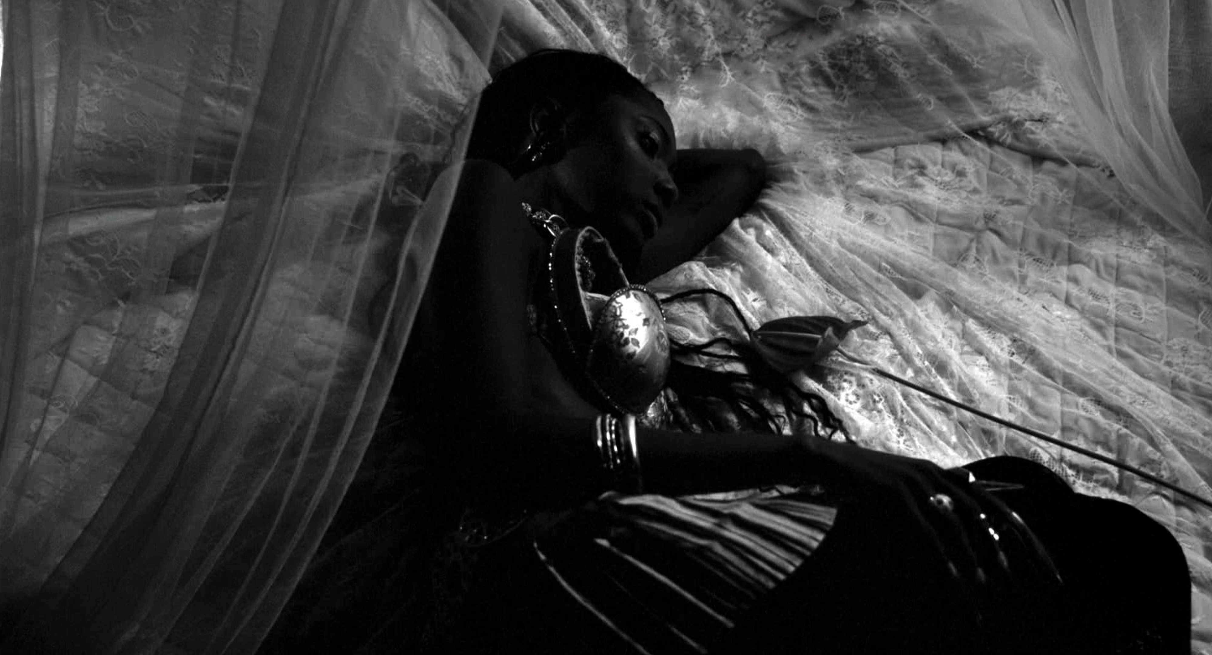 Black and white shot of a model with deep skin reclining on a bed